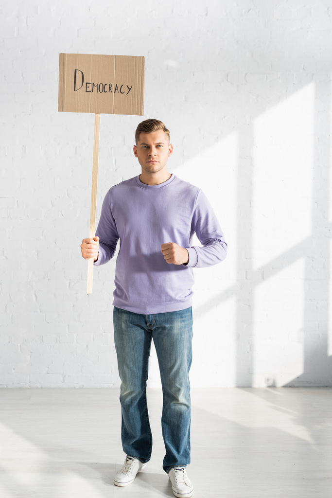 serious man holding placard with democracy inscription against white brick wall - Photo, Image