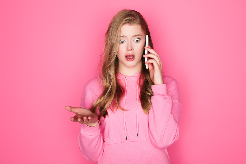 shocked beautiful woman talking on smartphone on pink background - Photo, Image