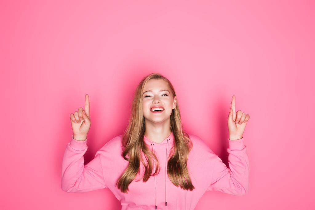 happy beautiful young woman in hoodie showing thumbs up on pink background - Photo, Image