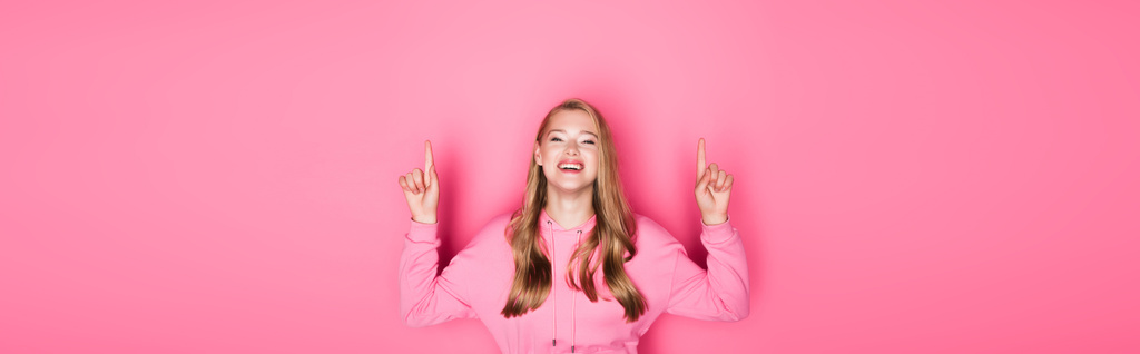счастливая красивая молодая женщина в капюшоне, показывающая большие пальцы на розовом фоне, баннер - Фото, изображение
