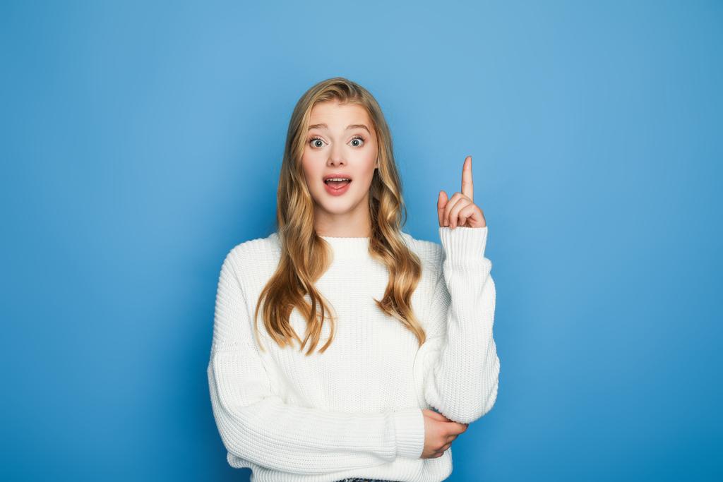 excited blonde beautiful woman in sweater showing idea gesture isolated on blue - Photo, Image