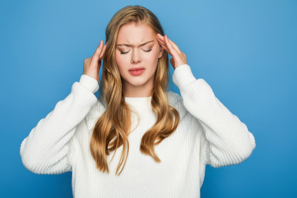 blonde beautiful woman in sweater having headache isolated on blue background - Photo, Image
