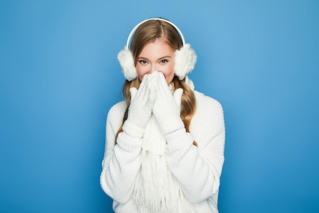 glimlachende mooie vrouw in de winter witte outfit geïsoleerd op blauw - Foto, afbeelding