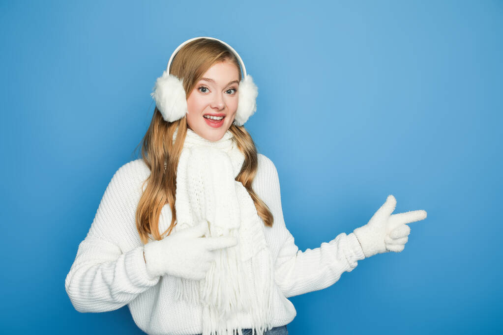 smiling beautiful woman in winter white outfit pointing aside isolated on blue - Photo, Image