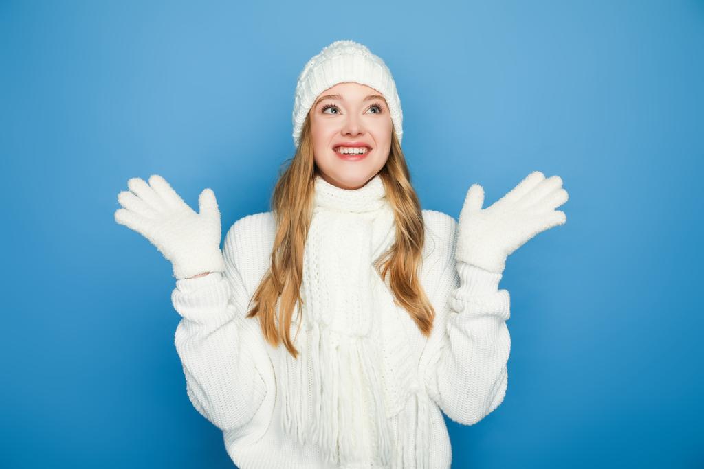 усміхнена красива жінка в зимовому білому вбранні ізольована на синьому
 - Фото, зображення