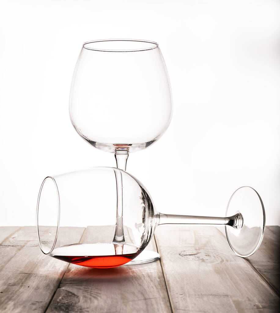 Δύο ποτήρια σε ένα λεπτό κοτσάνι σε λευκό φόντο, σε ένα απομεινάρι κόκκινου κρασιού. Ένα ποτήρι με λεπτό κοτσάνι και κόκκινο κρασί και ένα κεράσι στην άκρη. - Φωτογραφία, εικόνα