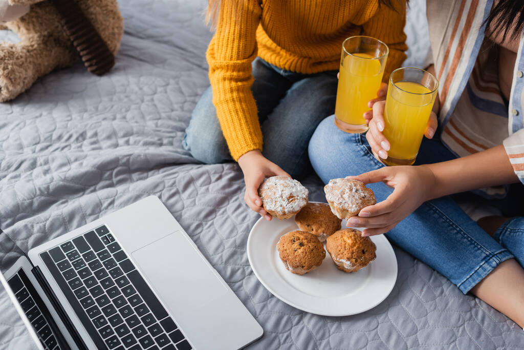 cropped view of mom and child holding orange juice and muffins while watching movie on laptop - Photo, Image