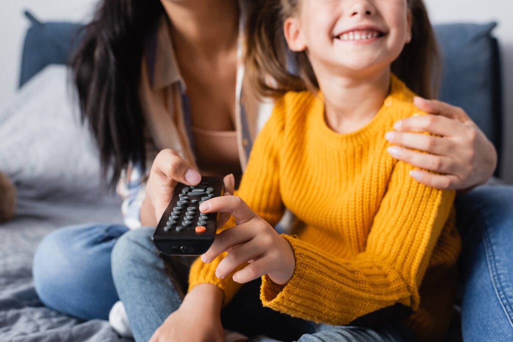 vista ritagliata di bambino felice guardando la tv con la madre su sfondo sfocato - Foto, immagini