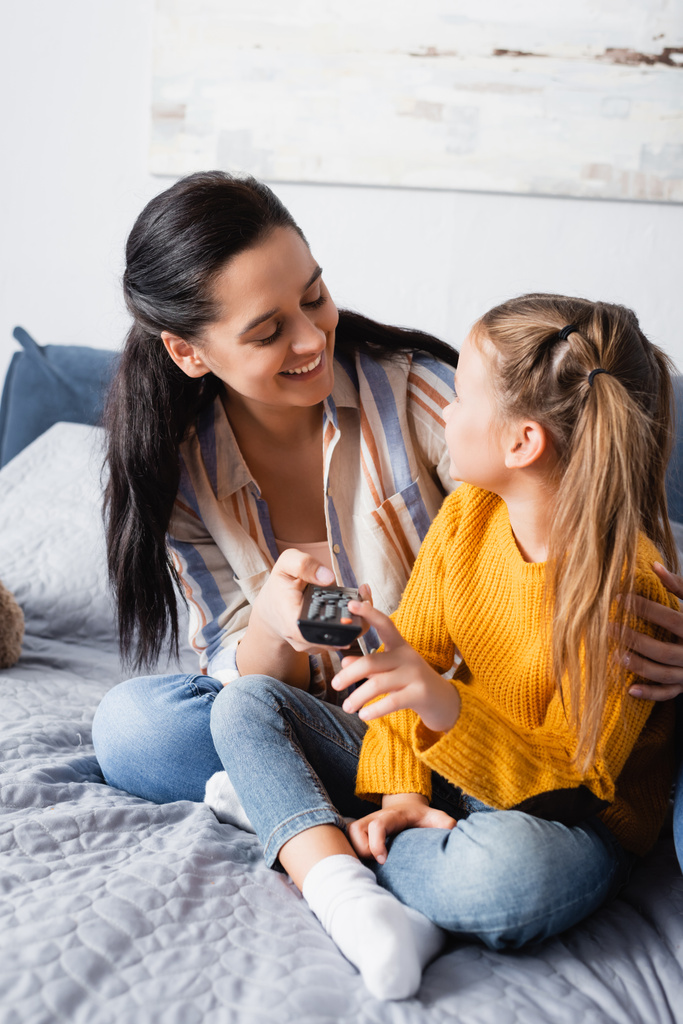 happy woman embracing daughter while holding tv remote controller - Photo, Image