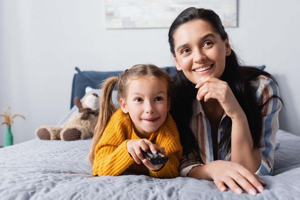 vzrušené dítě klikání kanály na dálkovém ovladači při sledování televize s matkou - Fotografie, Obrázek