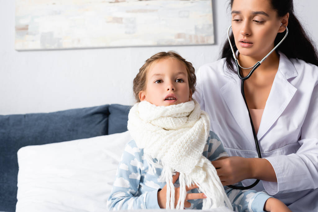 pediatrician examining girl, wrapped in warm scarf, with stethoscope - Photo, Image