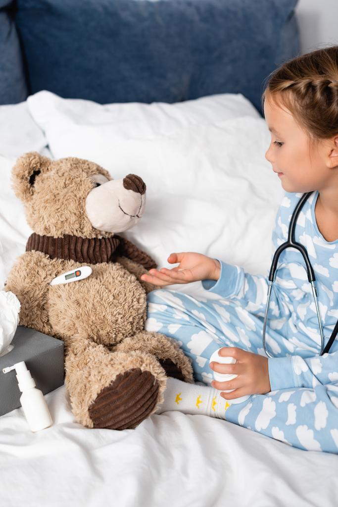 girl curing teddy bear while playing in bed - Photo, Image