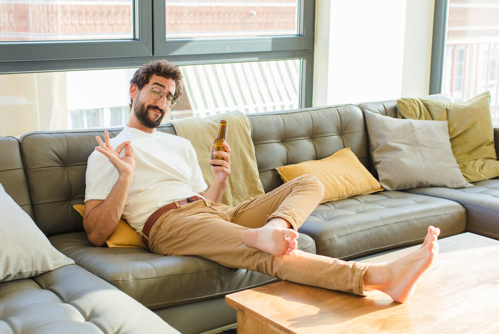 молодой бородатый холодный мужчина, сидящий дома на диване - Фото, изображение