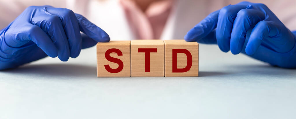 DST, Infecções sexualmente transmissíveis, texto acrônimo em cubos de madeira em mãos de médico em luvas na mesa azul cinza, banner - Foto, Imagem