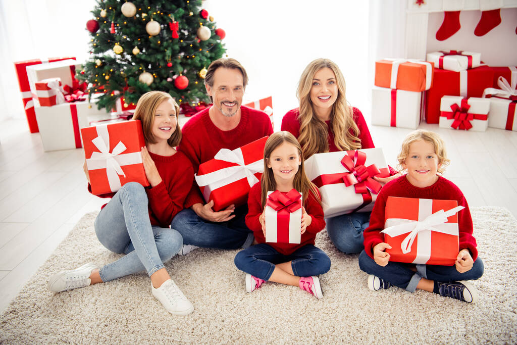 大きな家族の写真5人が集まる3人の小さな子供たちが床に座るカラフルなプレゼントを保持笑顔リビングルームで赤いジャンパージーンズxマスツリーガーランド多くのプレゼント屋内 - 写真・画像