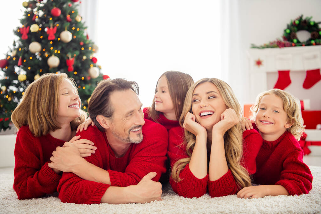Фотографія повної великої родини п'ять чоловік, що збирають трьох маленьких дітей лежать килим мама руки щоки веселі обійми носять червоний джемпер в прикрашеній вітальні Різдвяні ялинкові вогні в приміщенні
 - Фото, зображення