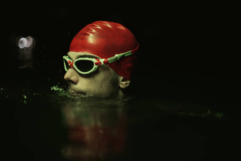 authentieke triatleet zwemmer met een pauze tijdens harde training op nacht neon gel licht - Foto, afbeelding