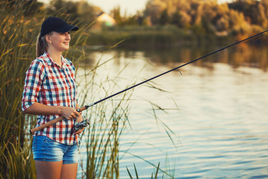 かわいい白人女性は夕日の夏の湖でロッドで釣りをしています - 写真・画像