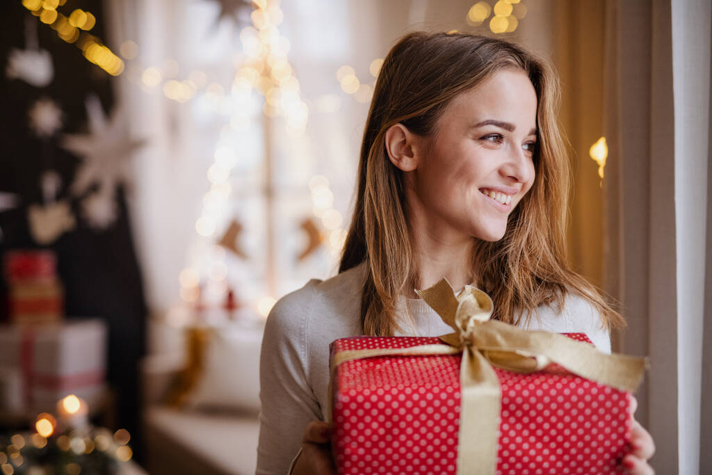 Giovane donna felice in casa a Natale, in possesso di regalo. - Foto, immagini