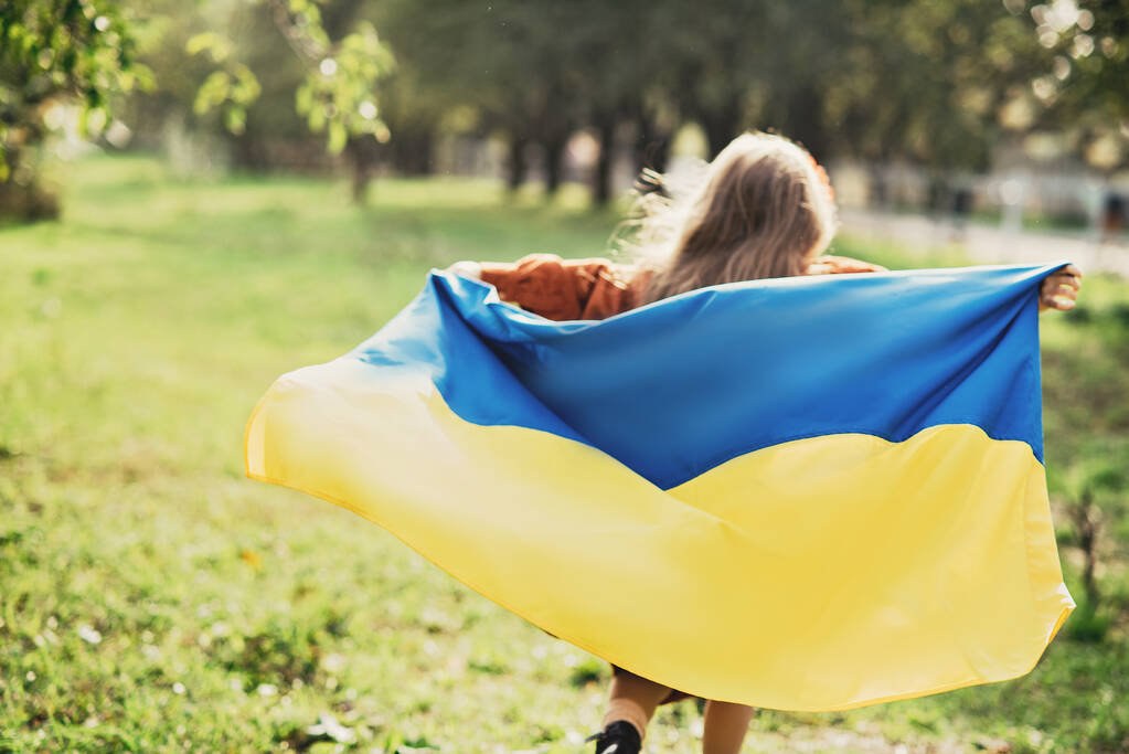 女の子はフィールドにウクライナのなびく青と黄色のフラグを運ぶ。ウクライナの独立記念日。憲法の日だ。8月24日。愛国的な休日. - 写真・画像