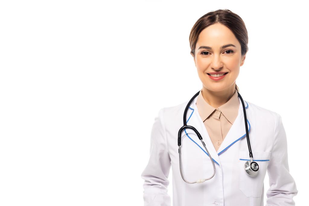 Pozitivní lékař v bílém plášti se stetoskopem při pohledu na kameru izolovanou na bílém - Fotografie, Obrázek