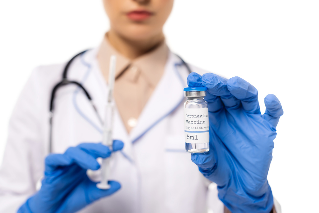 Ausgeschnittene Ansicht des Arztes in Latexhandschuhen mit Impfstoff mit Coronavirus-Schriftzug und Spritze isoliert auf weiß - Foto, Bild