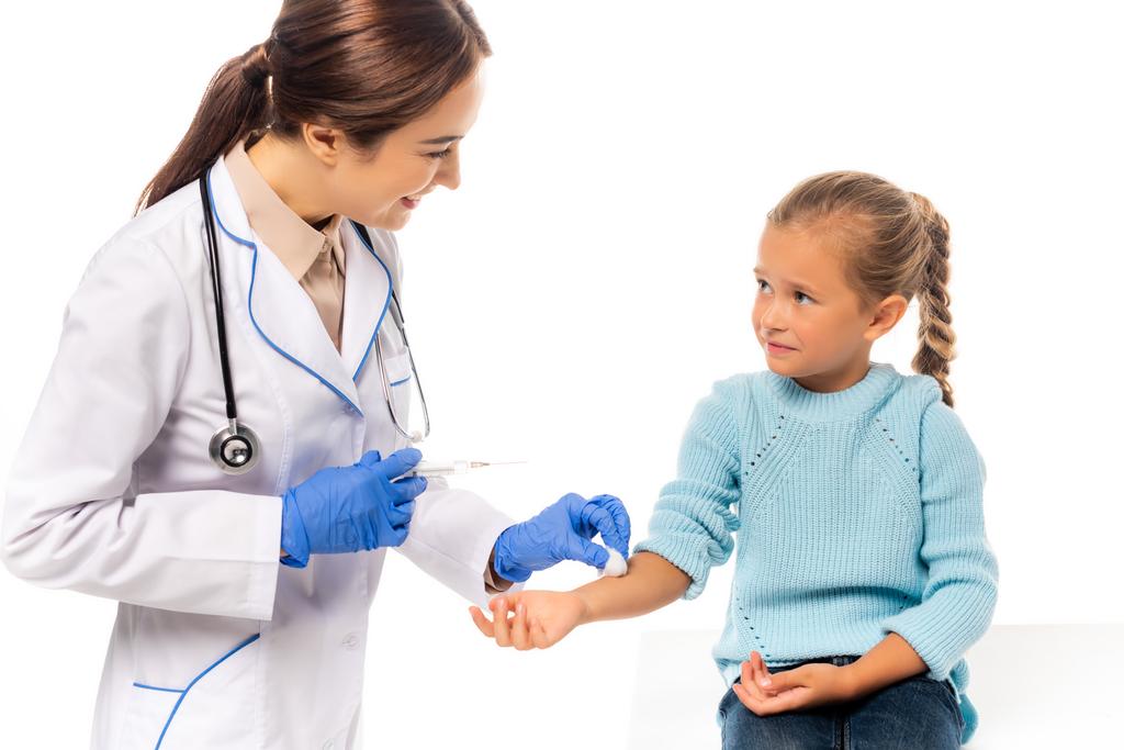 Smiling pediatrician holding cotton and syringe near child isolated on white - Photo, Image