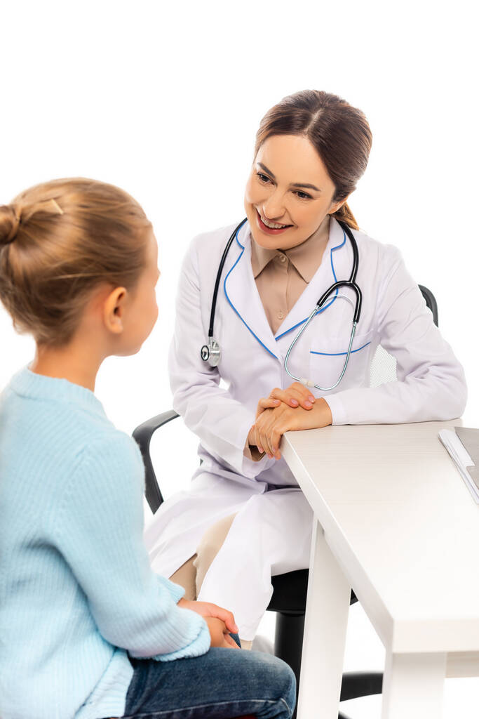 Valikoiva painopiste hymyilevä lastenlääkäri katsot tyttö lähellä pöytää eristetty valkoinen - Valokuva, kuva