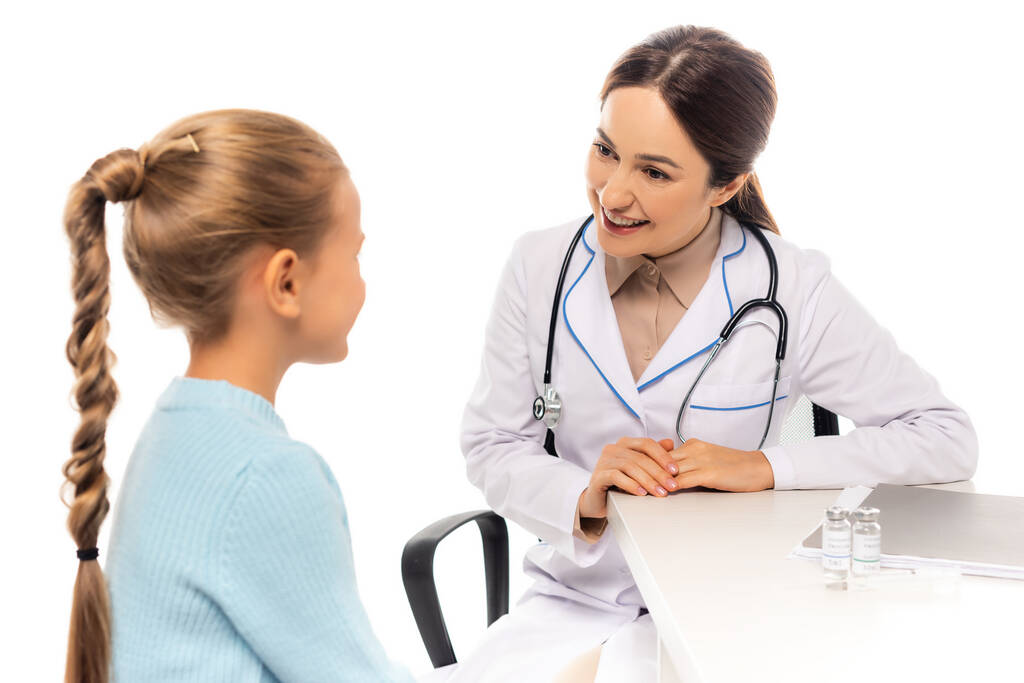 Selective focus of smiling pediatrician looking at child near vaccine and paper folder isolated on white - Photo, Image
