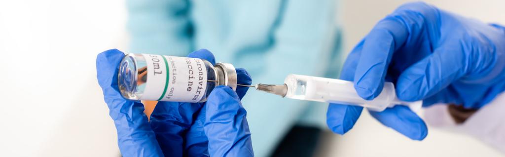 Panoramic crop of doctor in latex gloves holding syringe and vaccine with coronavirus lettering isolated on white - Photo, Image