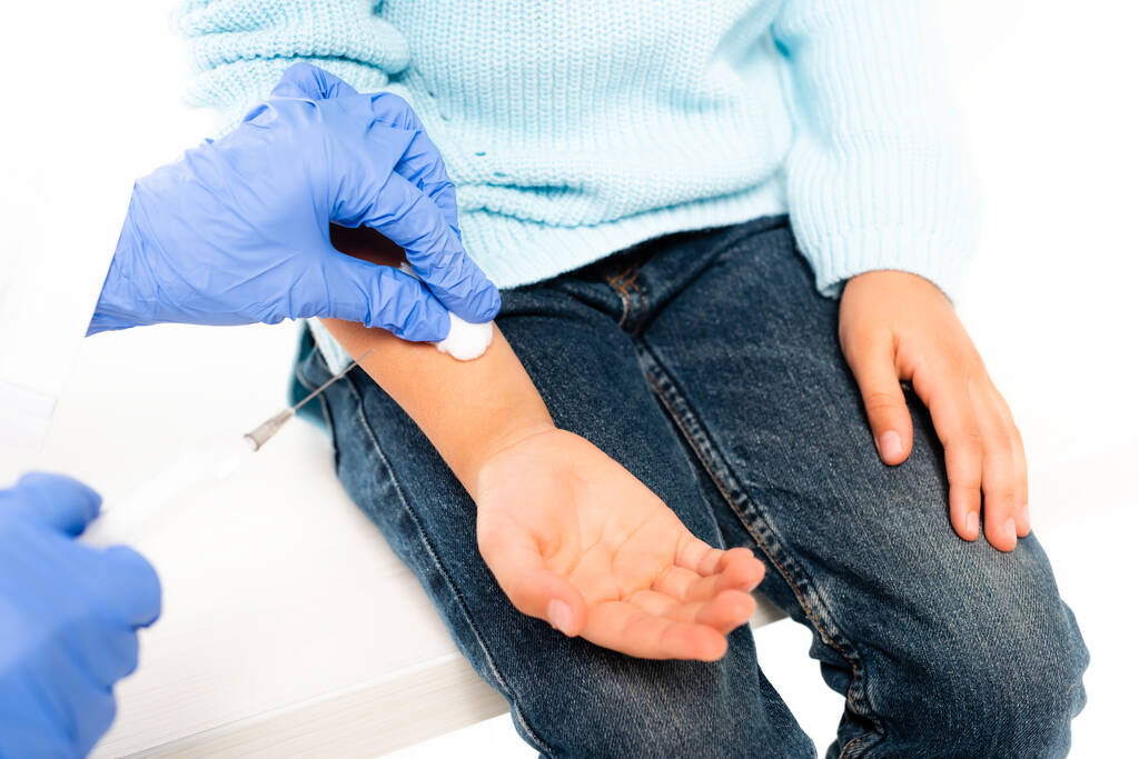 Vista recortada do médico segurando algodão e seringa perto da mão da menina isolada no branco - Foto, Imagem