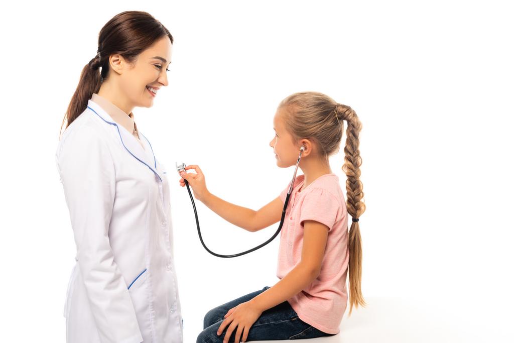 Dziecko trzymające stetoskop w pobliżu uśmiechniętego lekarza odizolowanego na białym - Zdjęcie, obraz