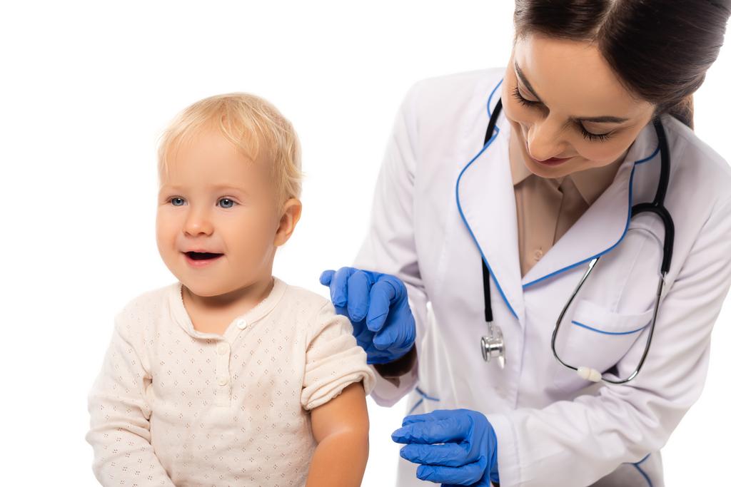 pédiatre en latex gants debout près joyeux tout-petit garçon isolé sur blanc - Photo, image