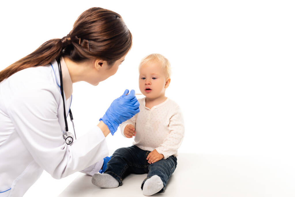Enfoque selectivo del médico sosteniendo palo cerca de niño pequeño aislado en blanco - Foto, Imagen