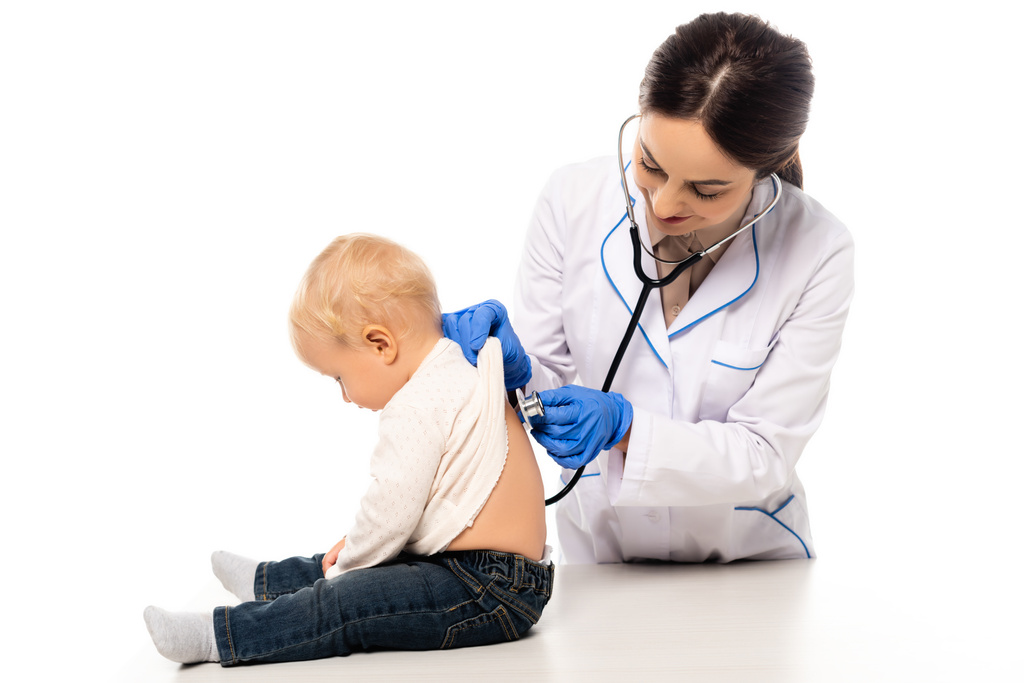 Pediatra sonriente examinando la espalda del niño pequeño con estetoscopio aislado en blanco - Foto, Imagen