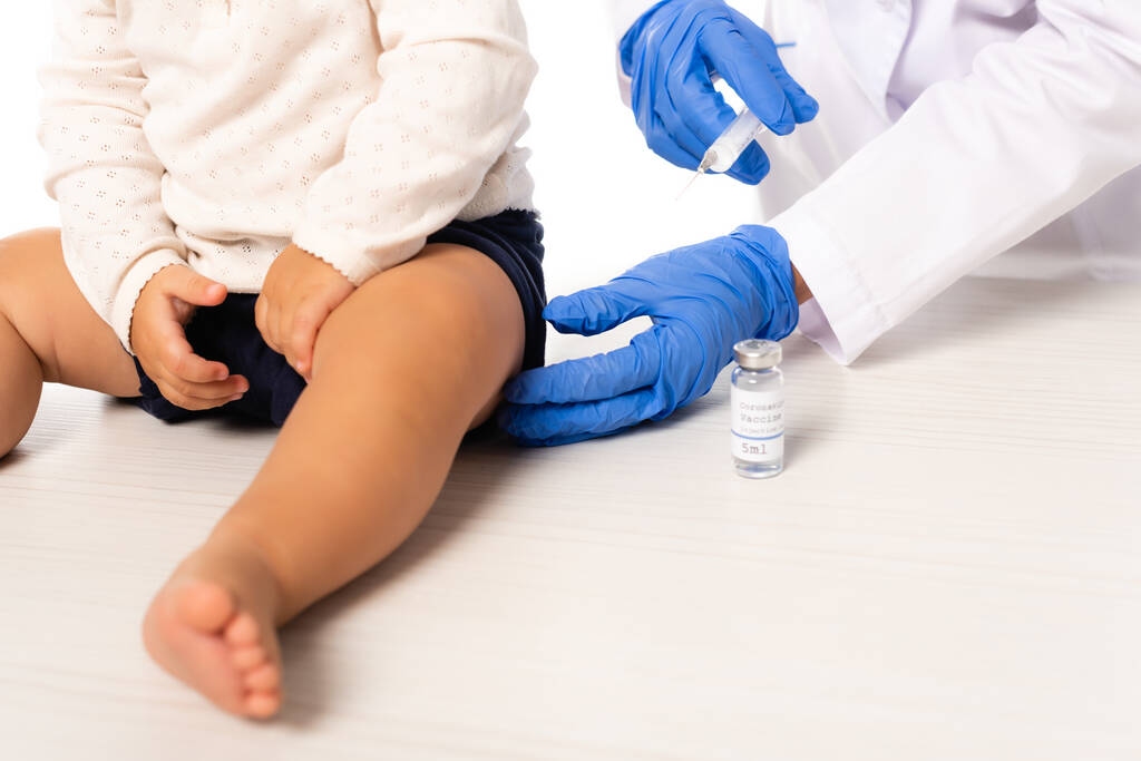 ワクチンの近くに注射器を保持小児科医と白に隔離された幼児の少年の作物ビュー - 写真・画像