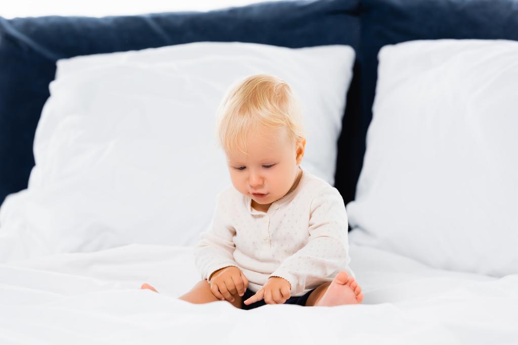 Batole chlapec ukazuje prstem, zatímco sedí na posteli na bílém pozadí  - Fotografie, Obrázek