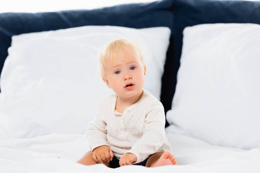 Selective focus of toddler boy looking at camera on bed on white background  - Photo, Image