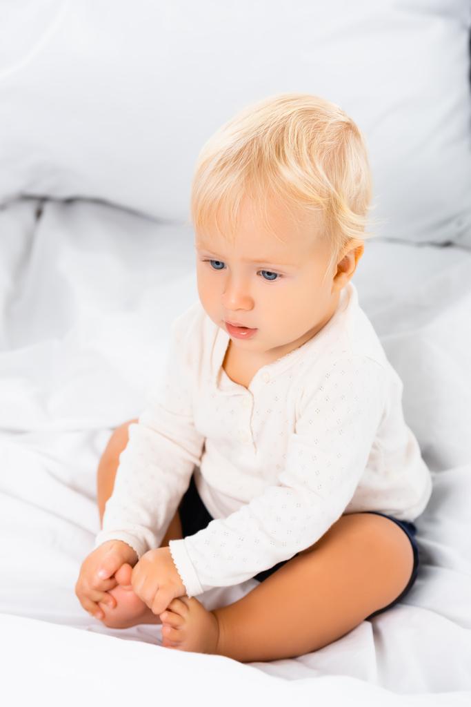 Selective focus of blonde toddler boy sitting on white bedding  - Photo, Image