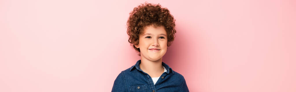 panoramic crop of pleased and curly boy in denim shirt smiling on pink  - Photo, Image