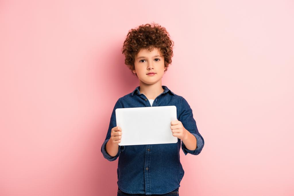 krullende jongen in denim shirt met digitale tablet op roze  - Foto, afbeelding