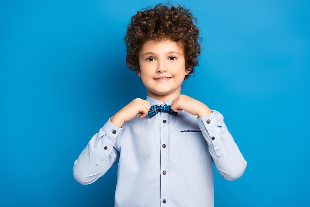 kudrnaté dítě v košili dotýká motýlka a usmívá se na modré - Fotografie, Obrázek