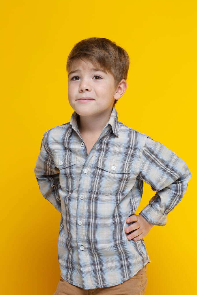 Симпатичный маленький улыбающийся мальчик в смокинговой рубашке, изолированный на желтом фоне.. - Фото, изображение