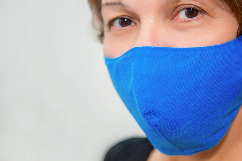 白い背景に保護再利用可能な手作りのマスクで中年の女性の肖像画。薬局における使い捨て医療用マスクの不足と再利用可能なマスクの人気の概念. - 写真・画像