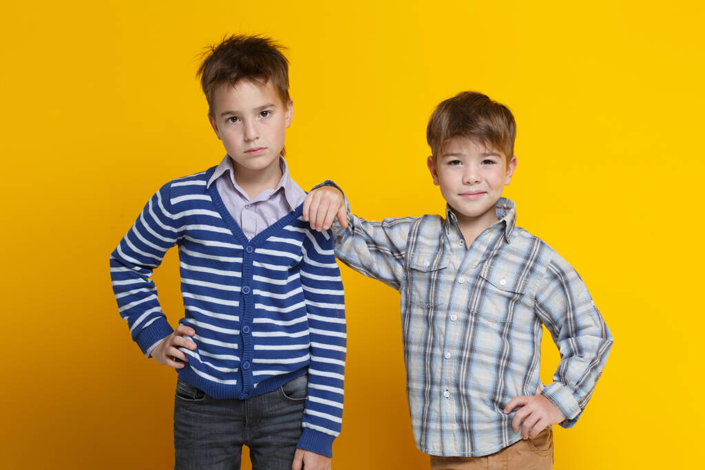 Deux drôles de petits garçons joyeux se tiennent côte à côte, l'un est appuyé sur l'épaule de la seconde, isolé sur un fond jaune vif. - Photo, image