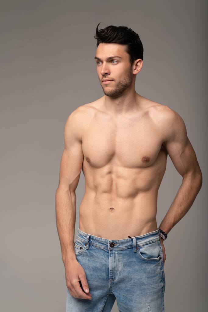 Portret van een goed gebouwd shirtloos gespierd mannelijk model tegen witte achtergrond. - Foto, afbeelding