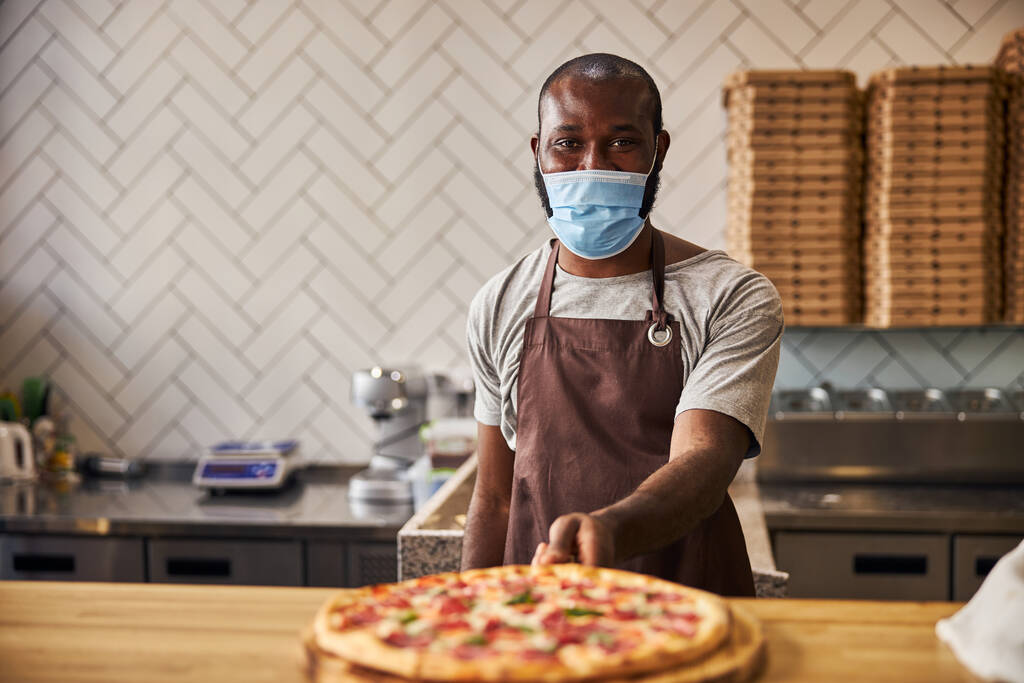 アフリカ系アメリカ人若いです男で医療マスク保持ペパロニピザ - 写真・画像