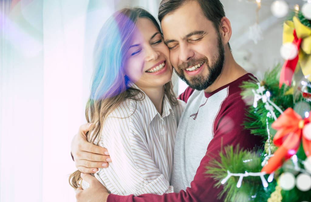 Nettes aufgeregtes glückliches Liebespaar umarmt sich und schmückt den Weihnachtsbaum im Winterurlaub zu Hause - Foto, Bild