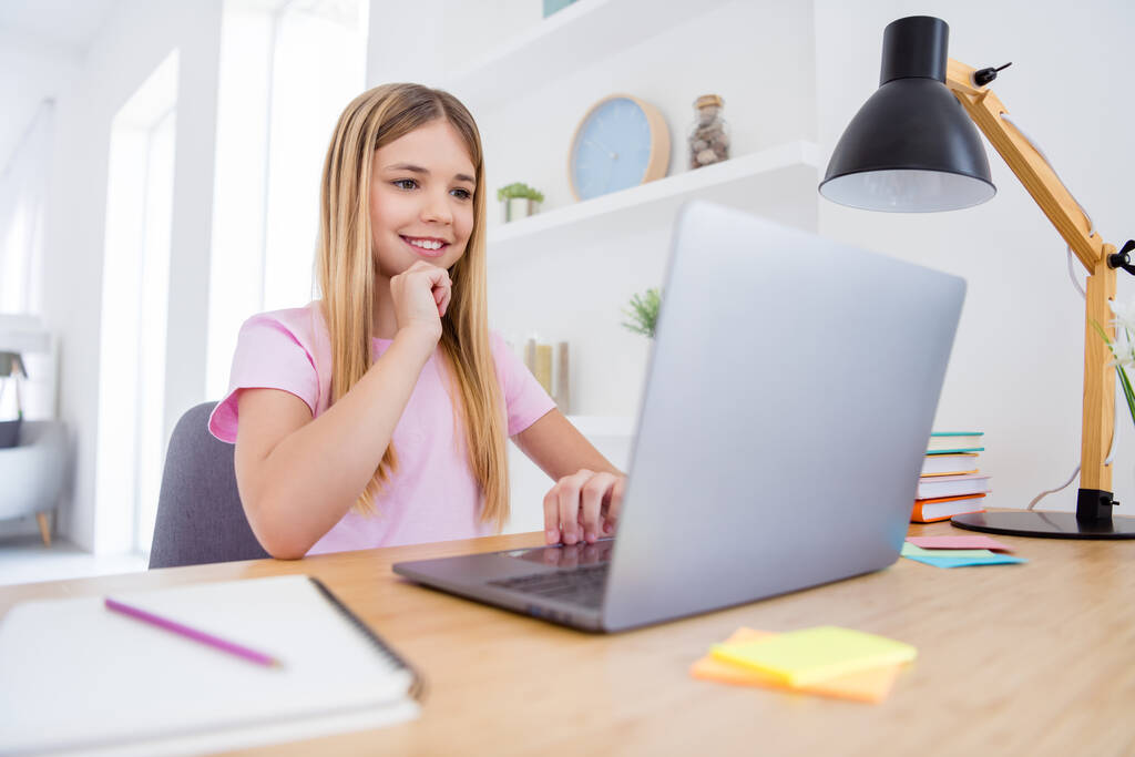 Foto van positief kind meisje zit tafel bureau studie op afstand gebruik laptop lezen onderwijs video webinar aanraking hand kin in huis binnen - Foto, afbeelding