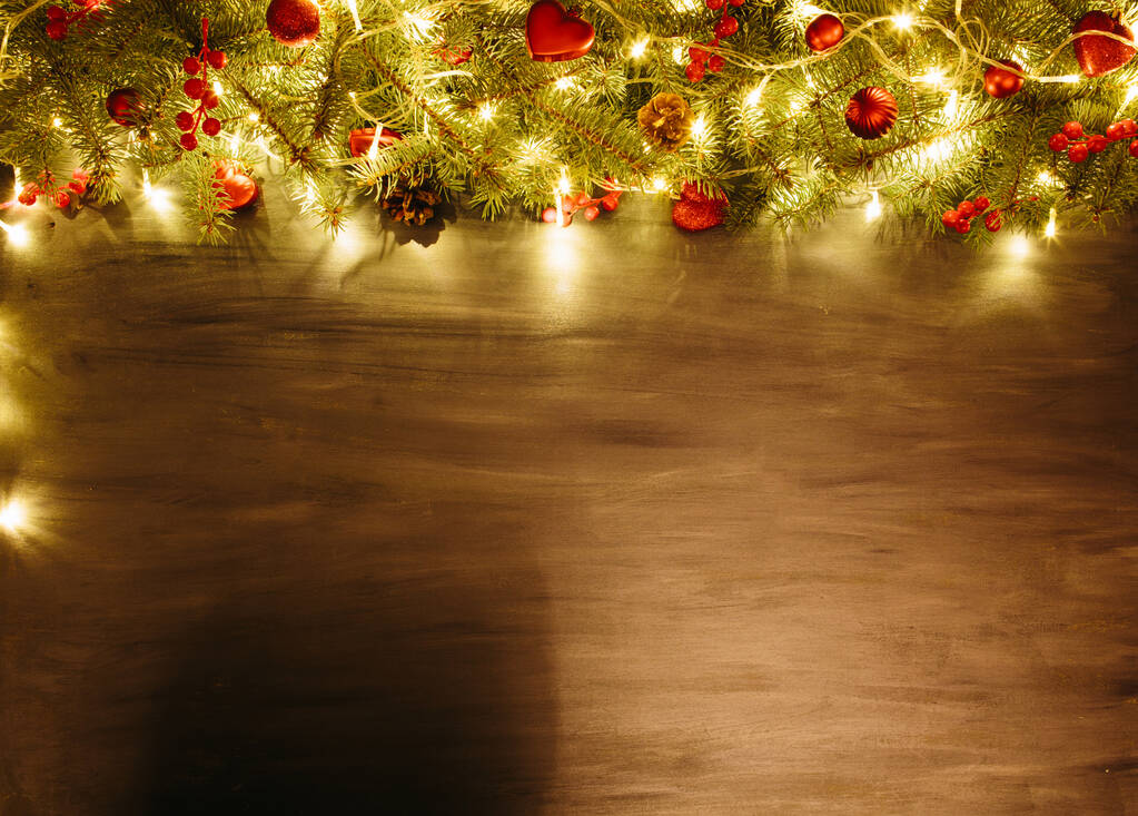 Šedé dřevěné vánoční pozadí s jedlovou větví a červenými vánočními ozdobami v rohu. Rámeček. Pohled shora - Fotografie, Obrázek